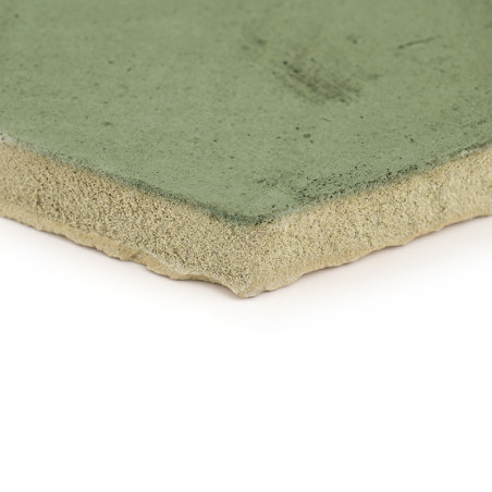 Una baldosa de terracota vidriada en verde descansa sobre un fondo blanco, con los bordes ásperos y sin terminar expuestos.