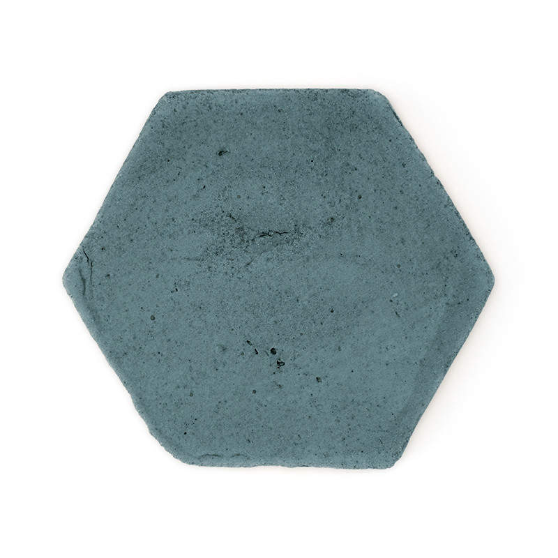 Zeshoekige terracotta tegel die plat ligt en een blauwgroen kleur vertoont met een subtiele oppervlaktetextuur, afgezet tegen ee