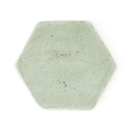 Baldosa de terracota hexagonal, apoyada sobre un fondo blanco liso, mostrando una superficie lisa de color gris claro con textur