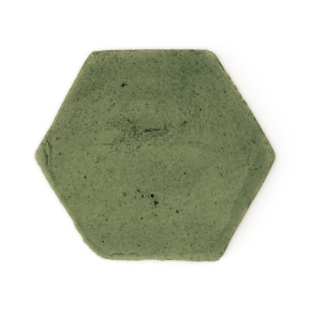 Carreau hexagonal en terre cuite, reposant à plat, avec une surface verte rugueuse et sourde, sur un fond blanc uni.