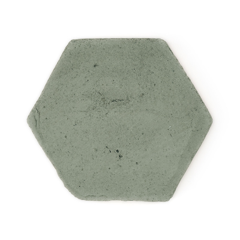 Zeshoekige terracotta tegel die plat ligt en een glad, gedempt groen oppervlak vertoont, afgezet tegen een effen witte achtergro