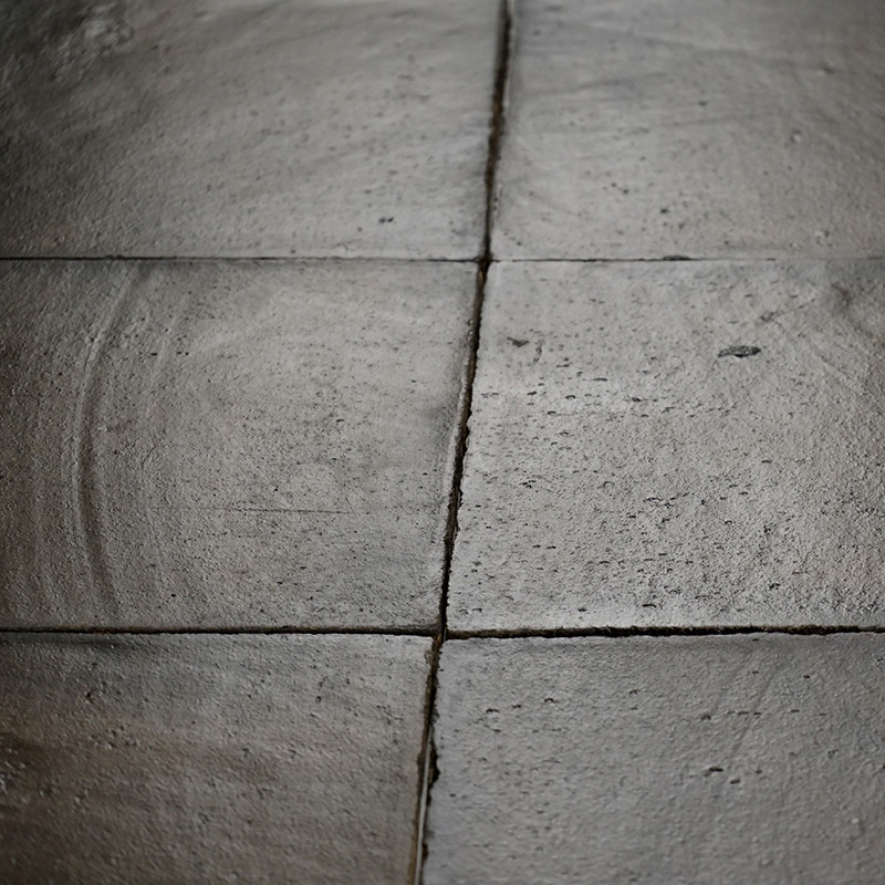 Azulejos cuadradas de terracota se encuentran adyacentes, sutilmente texturizadas con patrones circulares, formando un piso desg