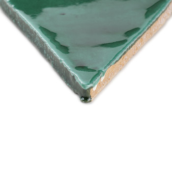 Auf einem weißen Hintergrund liegt eine grün glasierte Terrakottafliese, die ihre glänzende Oberfläche und die unglasierte Tonun