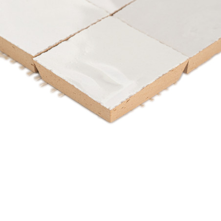 A white glazed terracotta tile resting on a plain white surface, showcasing texture and square shape with visible edges. A white glazed terracotta tile resting on a plain white surface, showcasing texture and square shape with visible edges.