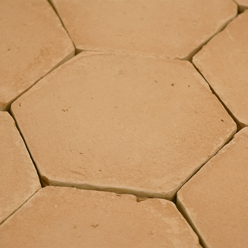 Zeshoekige terracottategels zijn dicht bij elkaar geplaatst, waardoor er kleine openingen zichtbaar zijn, waardoor een rustiek, 