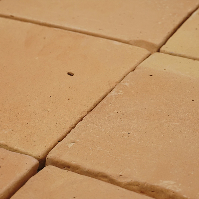 Terracottategels gerangschikt in een raster vormen een ruw, aards oppervlak, met kleine variaties in kleur en textuur.