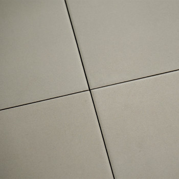 Four beige tiles meet with narrow, dark grout lines forming a cross pattern. the surface appears smooth and matte in a neutral s