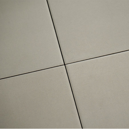 Four beige tiles meet with narrow, dark grout lines forming a cross pattern. the surface appears smooth and matte in a neutral s
