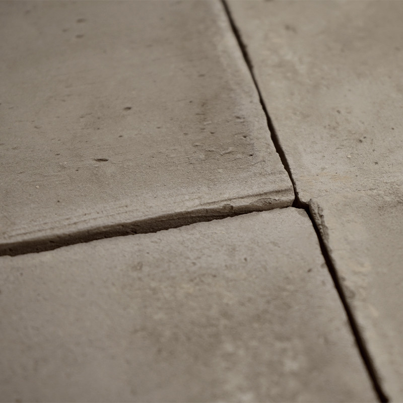 Four square terracotta tiles lie together, intersecting at the center, forming a textured flooring surface.