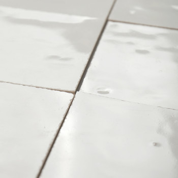 Witte terracotta tegels, glanzend en reflecterend, gerangschikt in een net rasterpatroon met zichtbare voeglijnen ertussen.