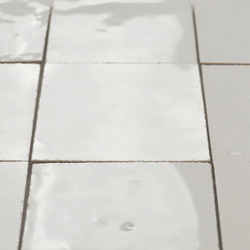 Glossy terracotta tiles are arranged seamlessly, with slight imperfections, reflecting light in a softly lit interior setting.