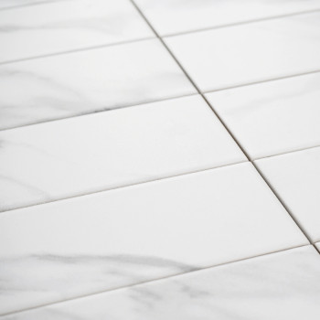 Les carreaux blancs rectangulaires avec de subtiles veines grises sont disposés selon un motif en grille, ressemblant à du marbr