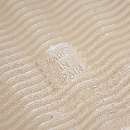 A sandy-colored tile features embossed waves, creating a textured appearance. In the center, the text `MADE IN SPAIN` is imprint A sandy-colored tile features embossed waves, creating a textured appearance. In the center, the text `MADE IN SPAIN` is imprint