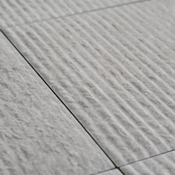 Gray ceramic tiles lie in alignment, featuring a textured surface with linear grooves, creating a subtle pattern across a flat f