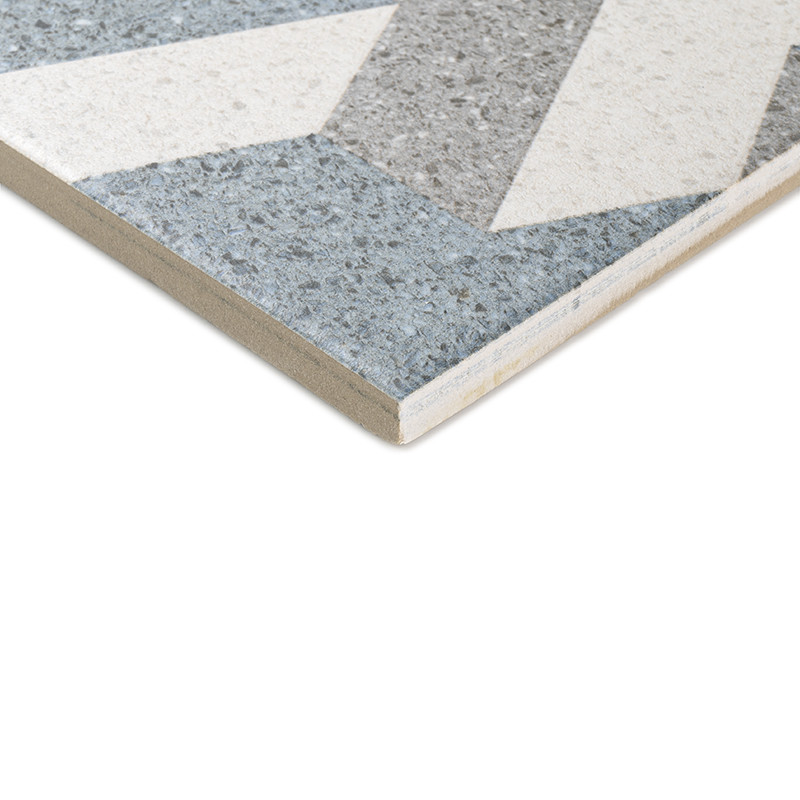Un azulejo cerámico con patrones geométricos con secciones grises, blancas y azules. El borde en ángulo del azulejo revela una e