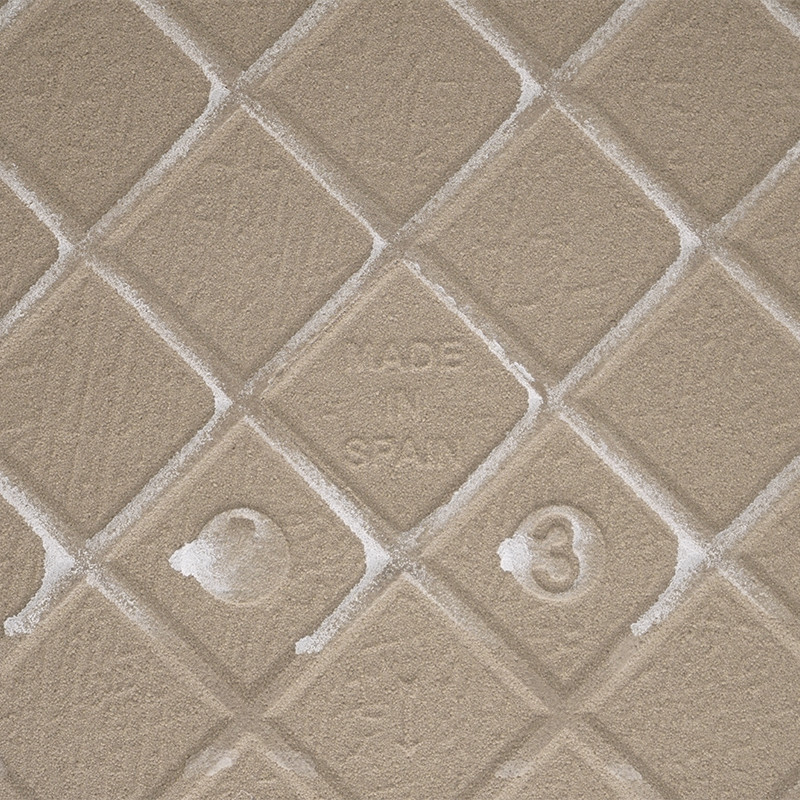 Eine beige, strukturierte Fliese mit einem erhabenen Rautenmuster zeigt in der Mitte „MADE IN SPAIN“, umgeben von subtilen Textu