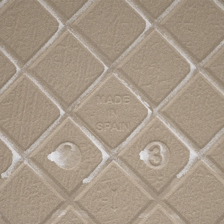 Eine beige, strukturierte Fliese mit einem erhabenen Rautenmuster zeigt in der Mitte „MADE IN SPAIN“, umgeben von subtilen Textu