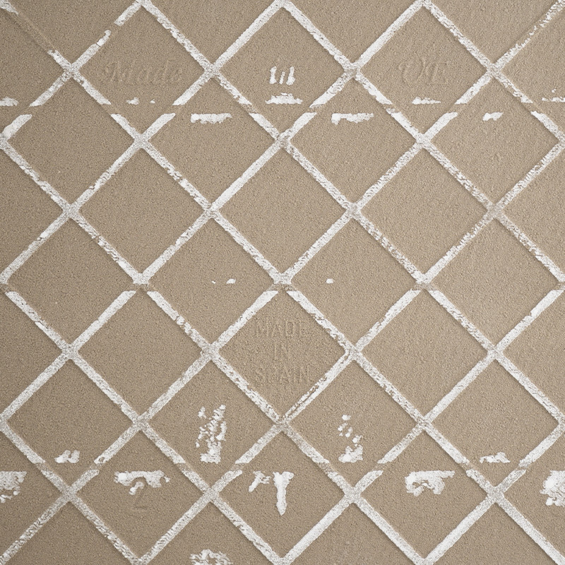 Un azulejo de cerámica beige muestra una cuadrícula de líneas blancas elevadas que se cruzan, formando formas de diamantes. El t
