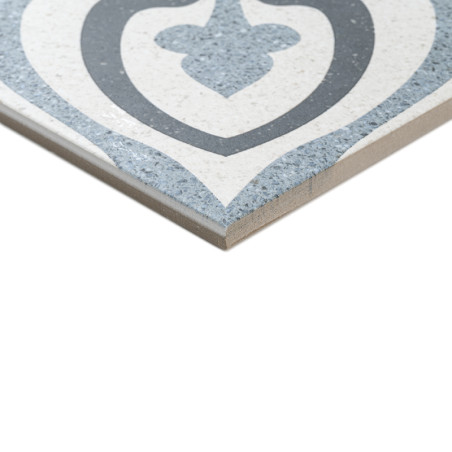 Un carreau de céramique affiche un motif géométrique symétrique aux tons gris et bleus, avec une forme de cœur centrale. Il est 
