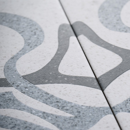 Deux carreaux de céramique avec des motifs abstraits gris et lisses imbriqués affichés sur un fond légèrement moucheté. Les moti