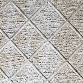 Erhabene beige Fliesen mit Rautenmuster weisen leichte Gebrauchsspuren auf, mit dem Text „1/1/03 mk sr“ auf einer Fliese, wodurc