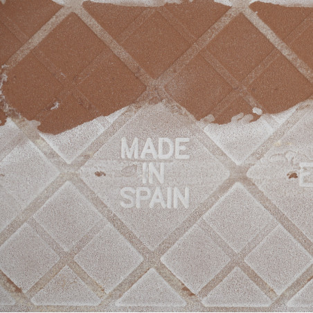 Een vierkante tegel met textuur, met in het midden de woorden `MADE IN SPAIN` in reliëf, met een geometrisch patroon. Stof bedek