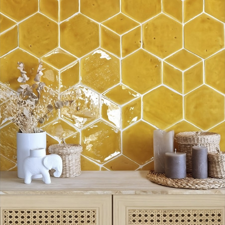 Azulejos hexagonales de terracota amarilla forman una pared texturizada sobre una mesa de madera con velas y elementos decorativ