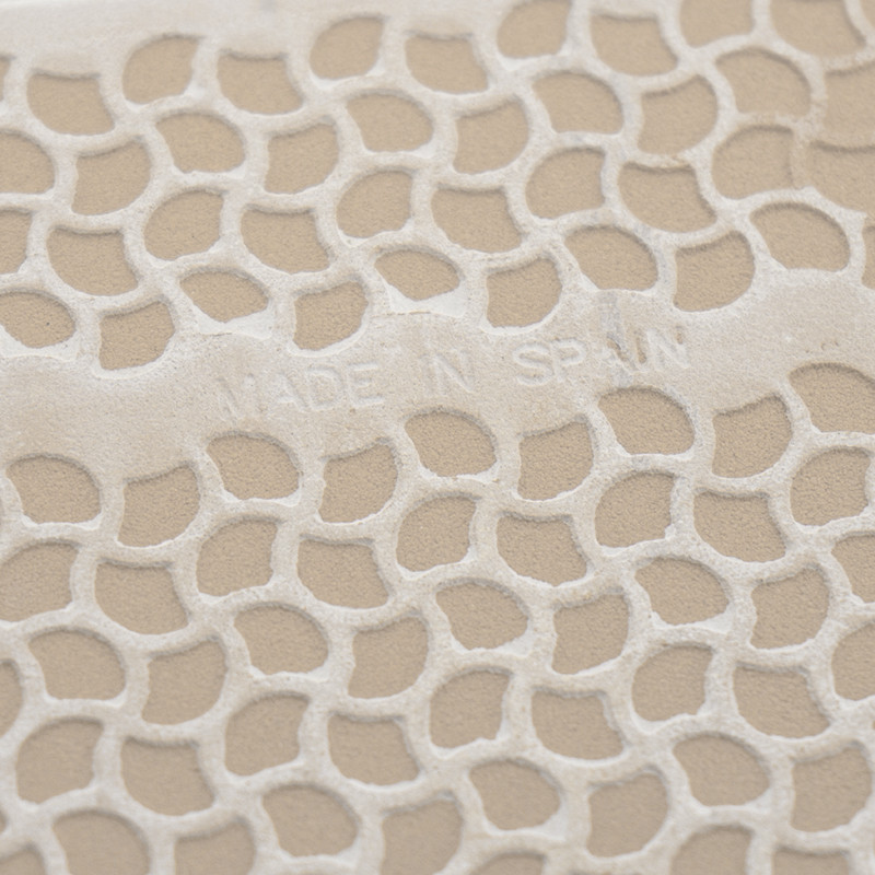 Carreau texturé avec motif en nid d'abeille en relief, affichant le texte « MADE IN SPAIN ». La surface a un fond beige.