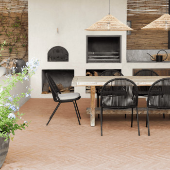 Terracottategels bedekken een patio met een houten eethoek, onder strolampen, met een kleioven tegen witte muren.