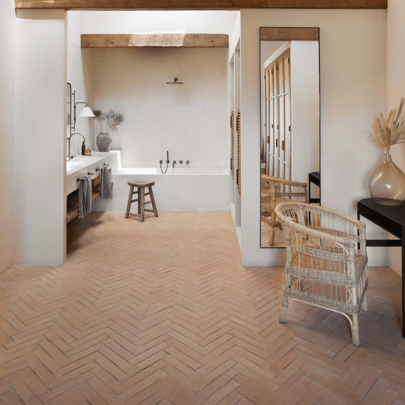Terracottategels bedekken de vloer, gerangschikt in een visgraatpatroon. ze versterken een rustieke badkamer met een lichte inri