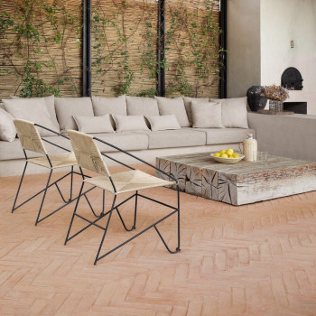 Terracotta tile floor supports black metal chairs and a stone table, in a cozy living space with beige furnishings.