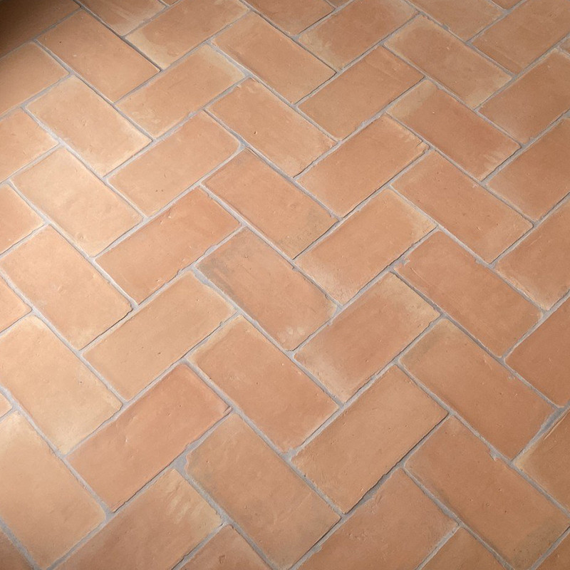 Terracottategels zijn gerangschikt in een visgraatpatroon, waardoor een rustieke vloer ontstaat in een warme, binnenomgeving.