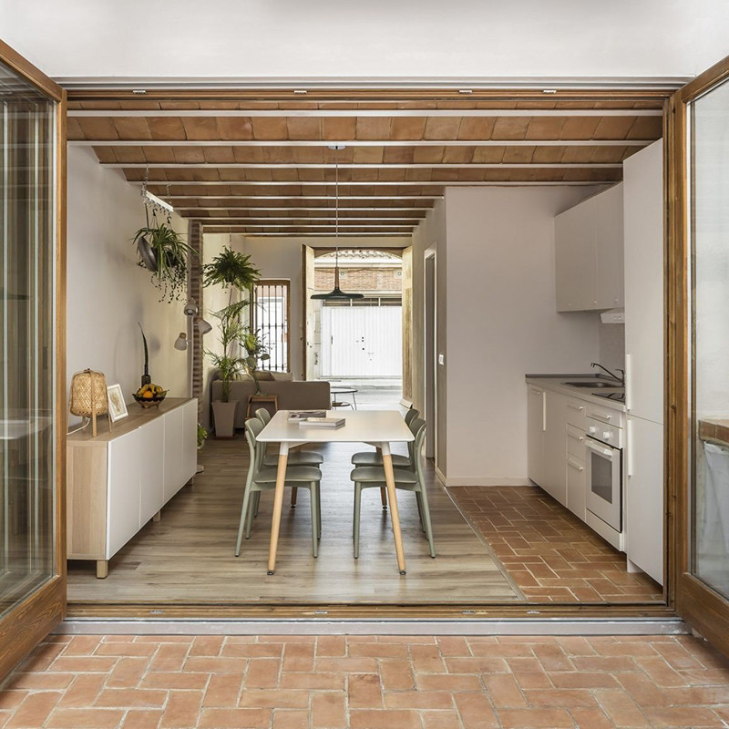 Ladrilhos de terracota formam um teto arqueado acima de uma cozinha moderna com armários brancos, mesa de jantar e área de estar