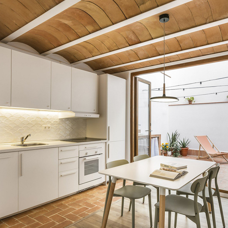 Terracottategels vormen een gewelfd plafond boven een moderne keuken met witte kasten, eettafel en aangrenzend zitgedeelte op de