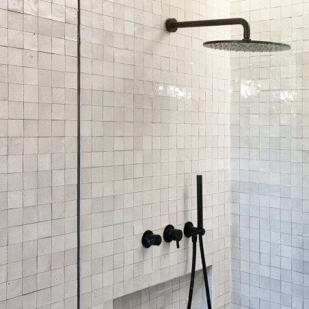 Showerhead protrudes from the wall, surrounded by glossy, square, white terracotta tiles in a modern, minimalist bathroom. Showerhead protrudes from the wall, surrounded by glossy, square, white terracotta tiles in a modern, minimalist bathroom.
