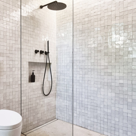 White terracotta tiles line a modern shower area, featuring a black rain shower head and handle, with glass enclosure. White terracotta tiles line a modern shower area, featuring a black rain shower head and handle, with glass enclosure.