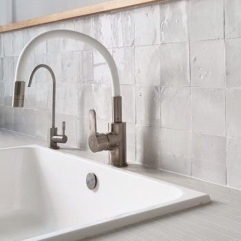 Robinet blanc incurvé sur évier blanc, entouré de carreaux en terre cuite blanche texturée sur un dosseret de cuisine moderne.