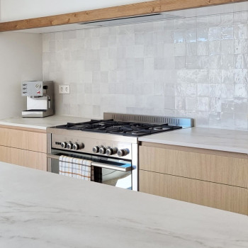 Torneira branca curva sobre pia branca, cercada por azulejos de terracota brancos texturizados em um backsplash de cozinha moder