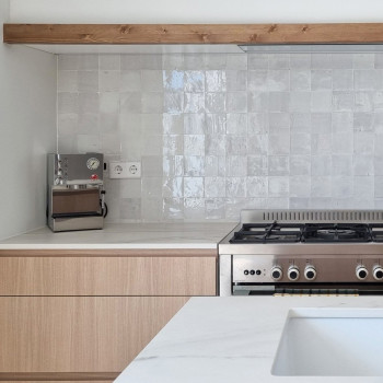 De achterwand van terracotta tegels weerspiegelt de verlichting onder de kast in een moderne keuken, omgeven door houten kasten 
