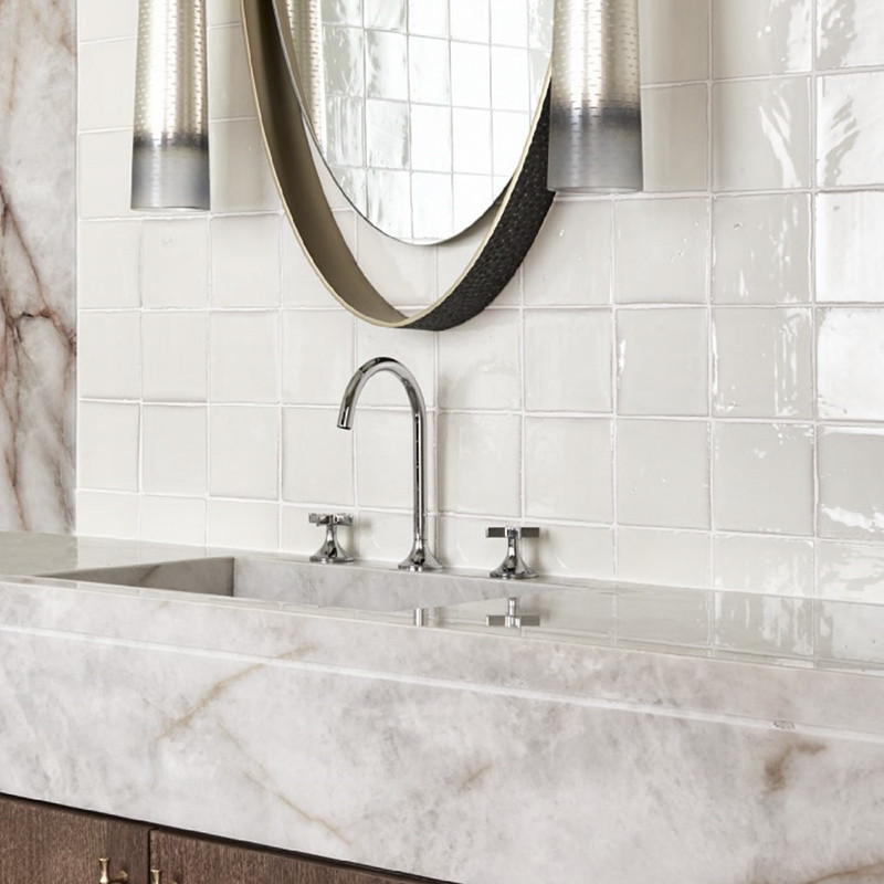 Los azulejos de terracota blanca se alinean en la pared del baño y reflejan la luz alrededor de una encimera de mármol con un gr