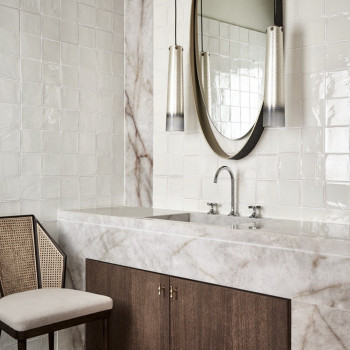 Des carreaux de terre cuite blanche recouvrent un mur de salle de bain, réfléchissant la lumière. lavabo en marbre en dessous, f