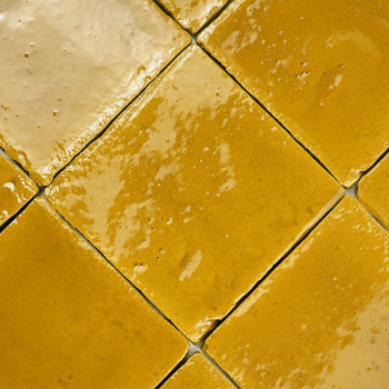 Glazed terracotta tiles arranged in a diagonal pattern, reflecting light, creating a warm, textured appearance in a bright setti