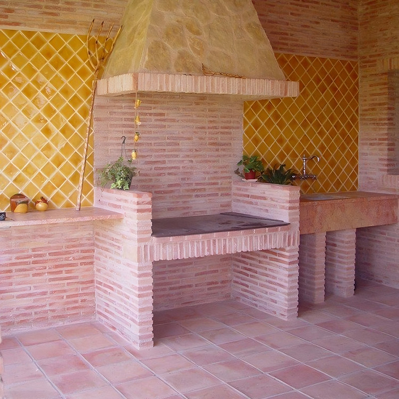 Terracottategels bedekken een rustieke barbecueplaats buiten, met muren met gele ruitpatronen, een steenoven en omliggende werkb