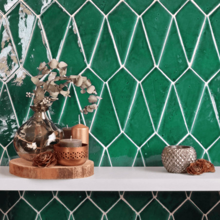 Green terracotta tiles form a geometric pattern. decorative vases and candles rest on a white shelf in front.
