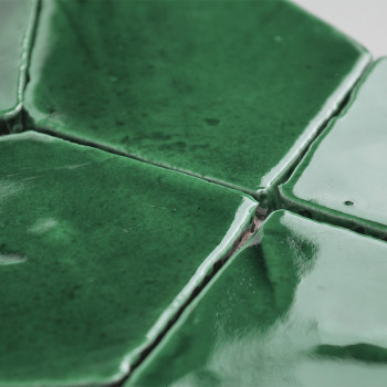 Groene terracottategels, samengevoegd en glanzend, vormen een structuurpatroon en vangen licht op in een close-up binnenomgeving