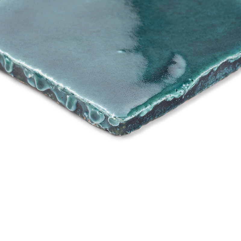 Un carreau en terre cuite verte vernissée présentant une texture dégoulinante. reposant sur un fond blanc, mettant en valeur sa 