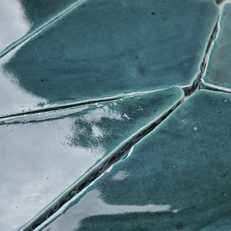 Geglazuurde blauwgroene terracottategels passen in elkaar en vormen een oneffen, reflecterend oppervlak met zichtbare voeglijnen