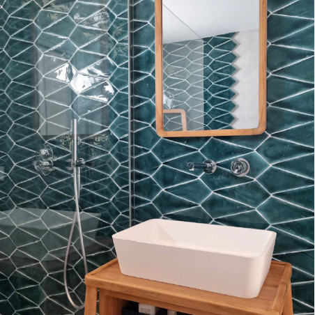 Een rechthoekige witte wastafel staat op een houten standaard, grenzend aan glanzende groene geometrische tegels in een badkamer