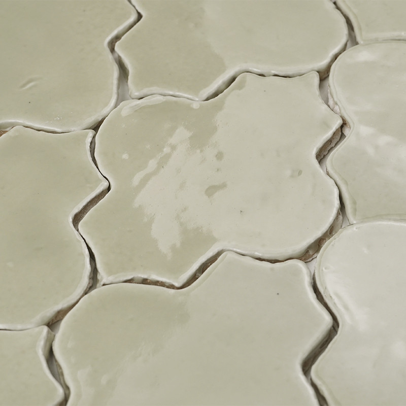 Crèmekleurige terracottategels vormen een bloemmotief, met glanzende oppervlakken die licht reflecteren in een overlappende opst