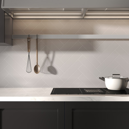 A white pot rests on a sleek stove beneath a row of hanging utensils in a modern kitchen with herringbone-patterned tiles.